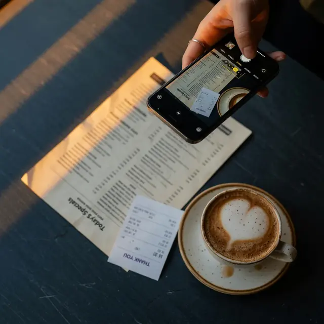 A hand photographing a cafe menu and receipt with a phone